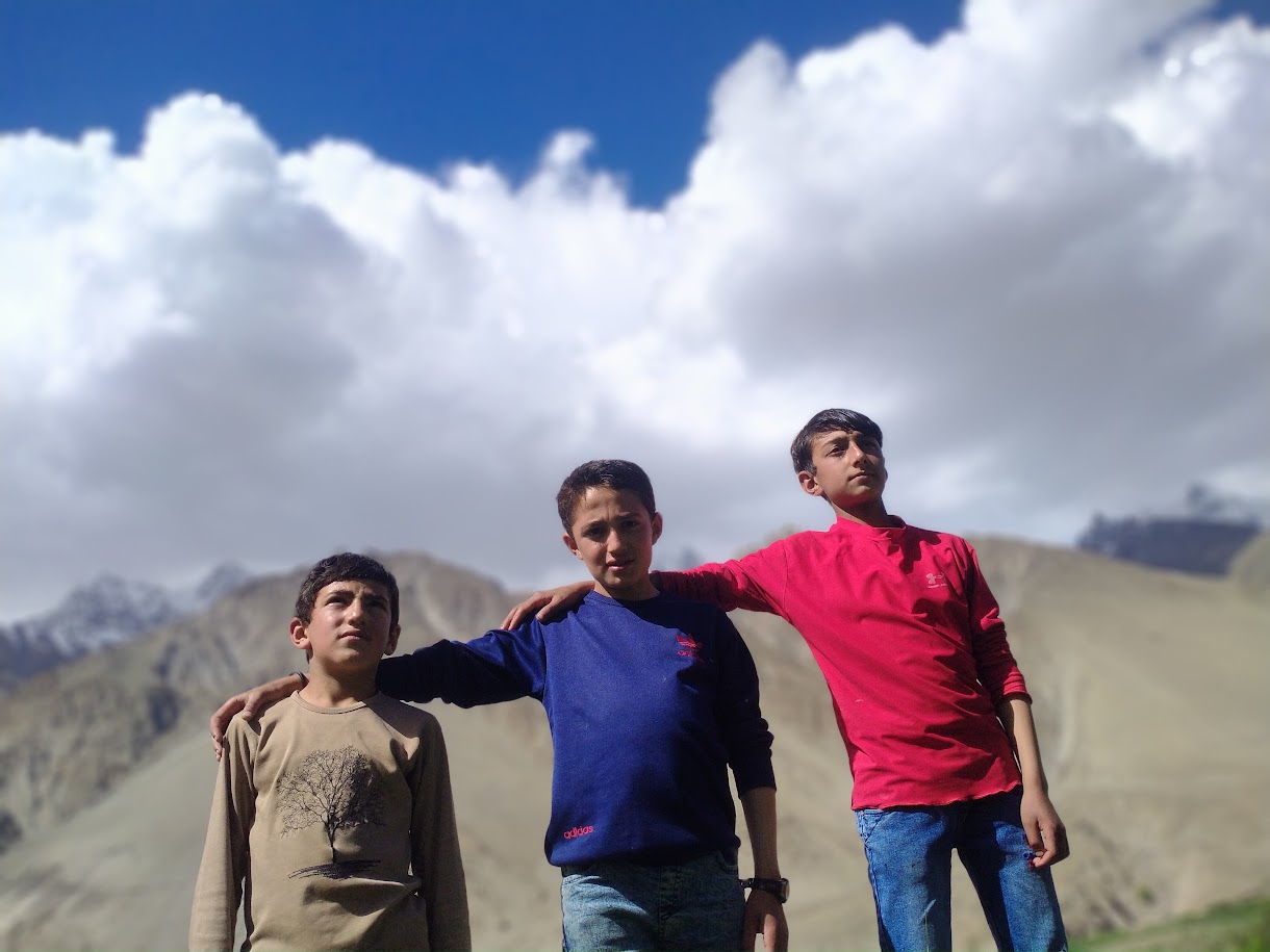 Three young Burusho community members posing in a mountain landscape, photographed by Abbas Ali